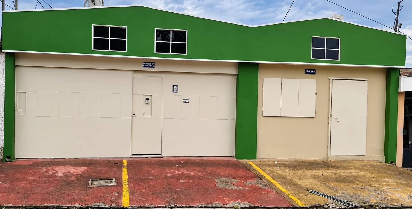 Fachada de CAPA: casa de pared verde con portón beige, número 16-A, con estacionamiento enfrente